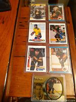 Seven vintage Vancouver Canuck rookie hockey cards laid out on wooden surface inside clear plastic sleeves.