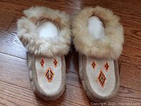 Pair of moccasins shown from top, featuring detailed beadwork and fluffy fur trim.