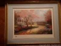 Framed print of Thomas Kinkade 'Morning Dogwood' with visible triple matting, wooden gilt frame, and glass covering. The painting shows a garden pathway and gazebo with blossoming dogwood trees and pastel colors.