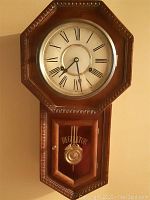 Front view of vintage oak regulator clock showing octagonal frame with Roman numeral dial and pendulum door with REGULATOR lettering.