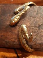 Close-up of the snake head ends showing textured scales and eyes on the brass bracelet.