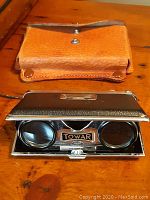 Brown leather carrying case with snap closure on wooden surface.