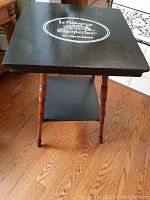 Full view of the table showing black painted top with text and oak legs.