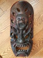 Front view of large dark brown hardwood TiKi tribal mask with carved roaring figure and leaf cutouts.