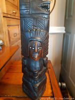 Front view of tiki totem showing carved face, headdress, and body details.