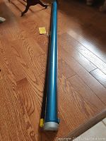 Full length photo of cylindrical blue metal casing of projection screen on wooden floor.