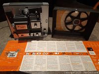 Front view of Bell & Howell 466BZ Autoload projector with attached manual spread out and empty film reel.