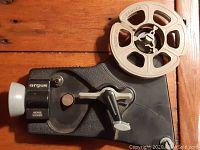 Top down view of Argus Movie Viewer with attached cream colored plastic film reel labeled 'Canada' showing main controls including crank handle and viewing lens.