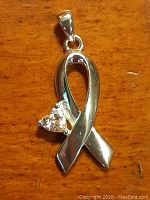 Close-up of silver ribbon-shaped pendant with a clear heart-shaped stone on wooden surface.