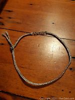 Full view of the sterling silver braided choker necklace laid flat on a wooden surface.