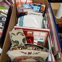 Top-down view of a box containing assorted holiday gift bags and Christmas gift boxes, including a 3-pack of gift boxes with red border and various holiday motifs.
