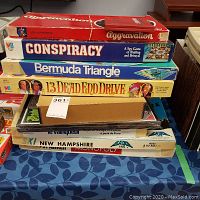 Stack of vintage board games including Aggravation, Conspiracy, Bermuda Triangle, and 13 Dead End Drive on a table.