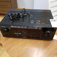 Front view of black Denon AV receiver on wooden table with power cord placed on top