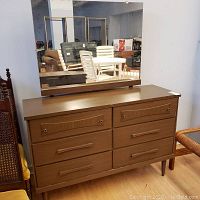Full view of 6 drawer dresser with mirror on top showing overall condition and style, brown wood laminate finish, horizontal wood handles, and mirror reflecting surrounding room.