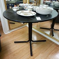 Full view of black round table showing the china set on top and the surrounding environment including mirrored wall and floor