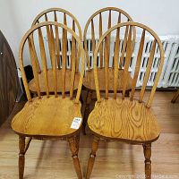Four oak spindle-back chairs arranged in a row showing front view.