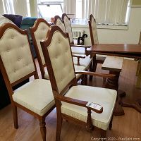 Photo showing side view of two dining chairs with cream tufted upholstery and wooden frame, and partial view of the dining table.