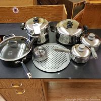 Set of Lagostina cookware items including skillet, double boiler, sauce pans, pot, steamer basket, and perforated pizza pan on black surface.