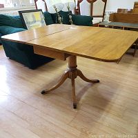 Wood drop leaf dining table with central pedestal base shown from side angle