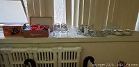Photo showing boxes with items and several drinking glasses, sherbet bowls, barware set in rack, and a Proctor Silex iron on windowsill.
