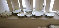 Wide angle showing all Noritake china pieces lined up, including plates, bowls, lidded serving bowl, and gravy boat.
