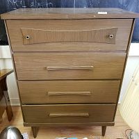 Front view of the chest showing four horizontal drawers with consistent light brown wood finish and decorative detail on top drawer
