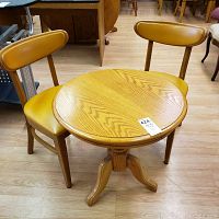 Round wooden table with two matching yellow cushioned chairs around it on a hardwood floor.