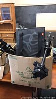 Camera tripods and equipment in cardboard box showing tripod legs and Gator case
