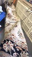 Rolled wool area rug with floral design along a radiator and cluttered room.