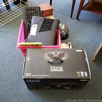 Pink storage bin containing Xbox 360 S console, Razer keyboard, headphones, computer speaker, and Xbox game cases with iHome iPod dock box in front.