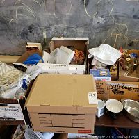 Boxes containing assortment of household items including decorative pieces, kitchenware, and media under chalkboard background