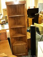 Wooden corner shelf unit with four triangular shelves and a bottom door with woven panel