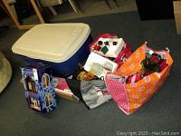 Photo showing the overall lot with a large blue plastic tote and reusable bags containing holiday decorations including the boxed musical house.