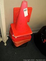 Stack of several orange traffic cones of standard design showing wear, some dirt, and a sticker on top cone.