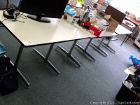 Side view of three matching rectangular tables with white tops and chrome T-shaped bases aligned together. Wear and chips visible on table surfaces.