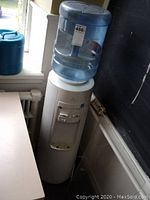 Front view of white Vitapur floor model water cooler with empty water jug on top next to a blue container.