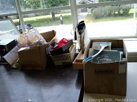 Wide view of cardboard boxes on table containing various office items including papers, pens, and tools