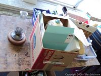 Photo of assorted items on a table including a box with Fitz and Floyd bunny candy jar and a basket of pet toys.