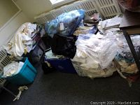 Multiple bags and bins filled with linens including towels, sheets, doilies, picnic tablecloths and other similar items.