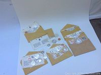 Six sealed coin sets in original cellophane sleeves displayed on white background with kraft envelopes