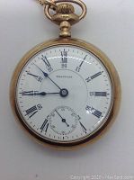 Front view of the watch dial showing white enamel face, Roman numerals, 24-hour inner track and blue steel hands
