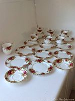 Overview of five cups on matching saucers, one mug, additional saucers and assorted plates arranged on white surface.