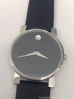 Close-up of black Museum dial with single dot at 12 o’clock and silver-tone hands