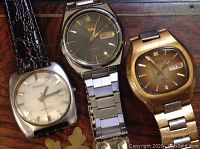 Three watches laid out side by side showing dials and straps