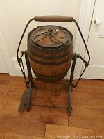 Front view of oak barrel churn mounted on iron frame showing yoke, handle, and barrel hoops