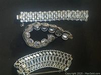Three antique bracelets laid out, one silver Avon sterling, one silver-tone with rhinestones marked Coro, and one unmarked silver-tone bracelet with rhinestones.