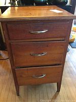 Front view of wooden side table showing three drawers with silver metal handles and visible wear on wood.