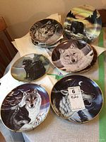 Eight 8-inch decorative plates with wildlife scenes and gold rims, stacked and displayed for sale. Includes wolves, bears, and other nature motifs.