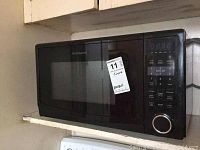 Frigidaire black microwave oven mounted, showing front control panel with buttons and dial knob, and label.