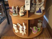 Round wooden shelf with grouped porcelain and ceramic figurines including dogs, clowns, and vases